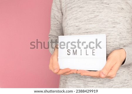 Word Smile. Female hands hold lightbox with letters in front of pink pastel background. 