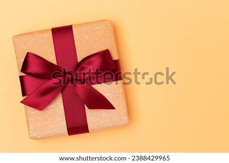 Gift box with red ribbon on a golden glittering background. Minimal festive composition with copy space.