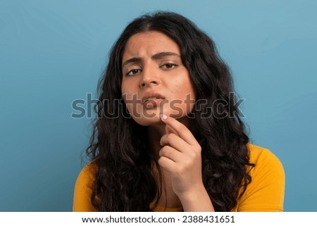 Stressed sad brunette young indian woman touching her face over blue studio background, having skin problems, closeup. Acne, pimples, wrinkles, dull skin Royalty-Free Stock Photo #2388431651