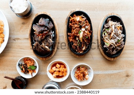 A feast of Korean BBQ with various meats and side dishes served on hot plates, accompanied by traditional banchan and steamed rice