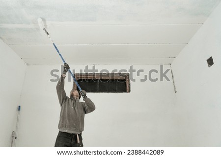 A skilled craftsman meticulously paints a pristine white ceiling using a telescopic roller for precise home improvement.