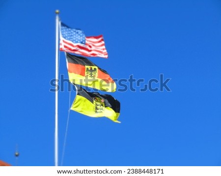 A picture of the U.S and German flag blowing in the wind together on a pole. 