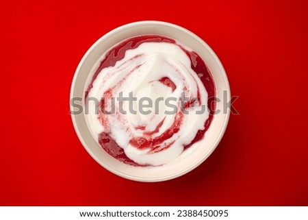 Bowl of yogurt with berry jam swirl on red background, top view