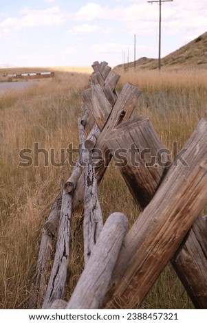 Various brown wooden split rail fences found across Montana.  Found against a background of blue cloud skies and surrounded by green grass, meadows and brown dried grasses. No people present. 