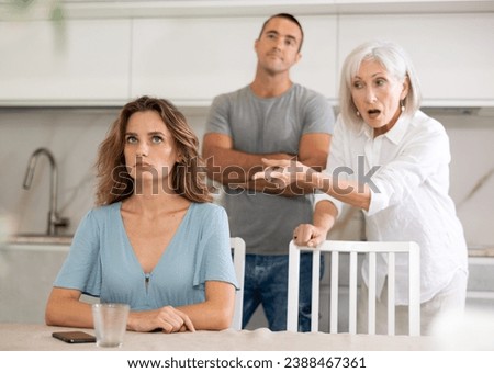 Adult man and elderly woman during family quarrel with adult woman in kitchen