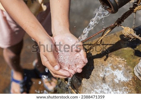 A young girl cradles refreshing water in her hands, poised to quench her thirst. Royalty-Free Stock Photo #2388471359