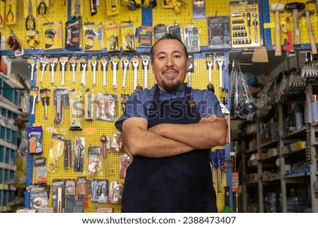 Handsome adult entrepreneur man in apron, with an expression of joy, happiness and proud in her business full of hardware products. Royalty-Free Stock Photo #2388473407