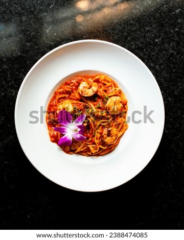 A plate of shrimp pasta with red sauce and a purple flower garnish, presented on a dark marble counter Royalty-Free Stock Photo #2388474085
