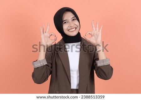 young asian beautiful muslim business woman with ok sign gesture approval sign wearing a brown suit isolated on peach background 