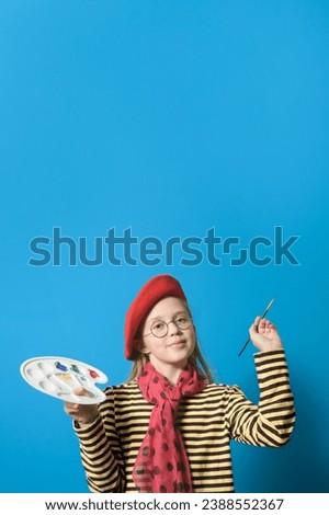 A young artist. A girl with a palette of colors in a bright red beret and with a brush on a blue background. vertical format