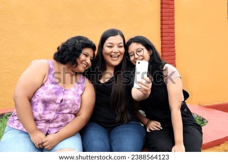 Young mom with her Latin daughters use cell phone to take selfies and make video calls