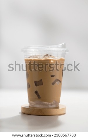 Iced cappuccino in a plastic glass on a white wooden table, minimalist-style picture.
