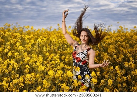 Beautiful Latina woman in floral dress with her hair flying in the wind in a canola field