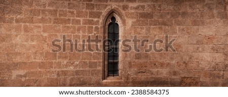 A medieval wall with a gothic window in the middle. Copy space for additional content on both sides. Royalty-Free Stock Photo #2388584375