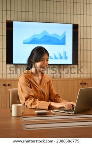 Charming Asian businesswoman sitting in meeting room and working on laptop computer.