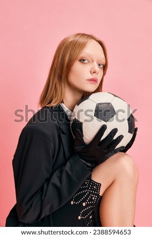 Half length portrait of young pretty woman dressed smart casual outfit in elegant gloves holding football ball isolated pastel pink background. Concept of active lifestyle, business, sport, hobby.