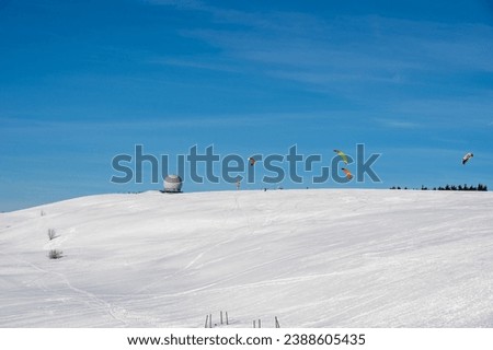 Snow kiting on the Wasserkuppe with radar dome in Germany on a beautiful winter day with blue sky and lots of snow Royalty-Free Stock Photo #2388605435