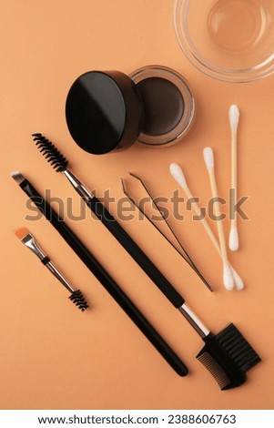 Eyebrow pomade with henna effect and professional tools on orange background, flat lay
