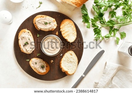 Chicken liver pate on toasted bread on wooden cutting board over light background. Top view, flat lay