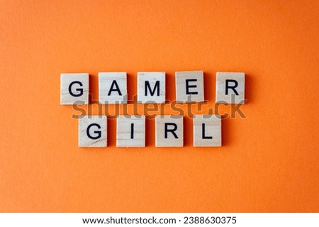 Word gamer girl. The phrase is laid out in wooden letters top view. Orange flat lay background