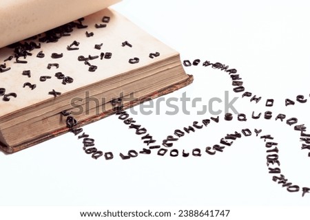 Old book and small letters. Black letters fall out of the book. White background. Royalty-Free Stock Photo #2388641747