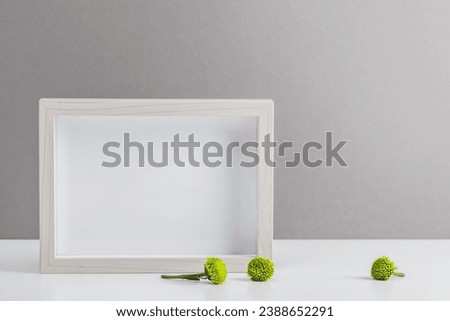 Photo frame on a gray background and small green chrysanthemums. Women's workplace, interior design, congratulations, mockup.