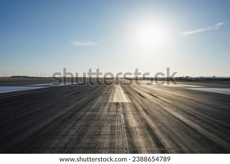 Surface level of long airport runway with directional marking against clear sky. 
