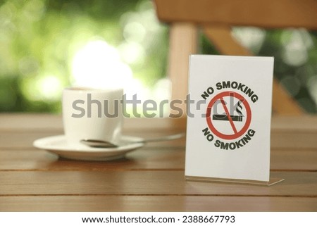 No Smoking sign and cup of drink on wooden table outdoors. Space for text