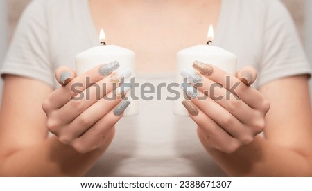 Female hands with long nail design. Glitter gold and white nail polish manicure. Female hands with perfect manicure hold candle.