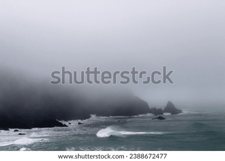 Rocks off route 101 coastal highway during a storm, Image shows the rough Pacific ocean swells hitting the cliffs and low level fog and mist covering the bay  Royalty-Free Stock Photo #2388672477