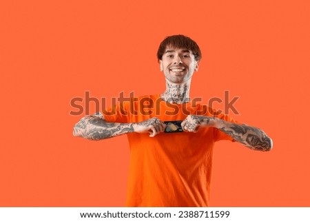Tattooed young man with credit card on orange background