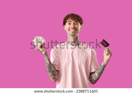Tattooed young man with credit card and cash on purple background