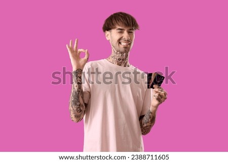 Tattooed young man with credit cards showing OK on purple background