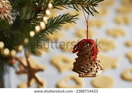 Bell shaped straw ornament hanging from a spruce tree branch, with raw Linzer Christmas cookies in the background