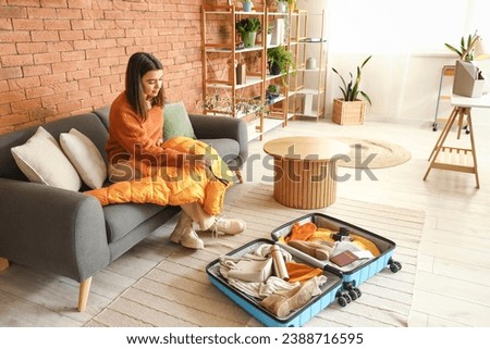 Young woman packing winter clothes in suitcase at home Royalty-Free Stock Photo #2388716595
