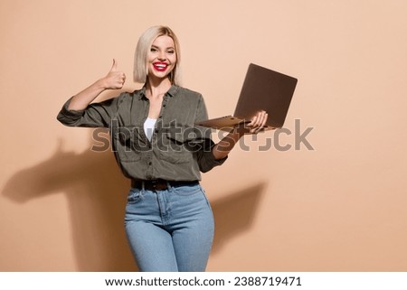 Photo of pretty cheerful woman dressed khaki shirt texting modern device thumb up empty space isolated beige color background