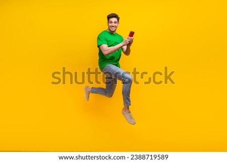 Full size photo of cool funny guy wear stylish t-shirt run to empty space with smartphone in hands isolated on yellow color background