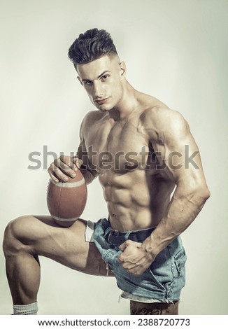 A shirtless man holding a football posing for a picture