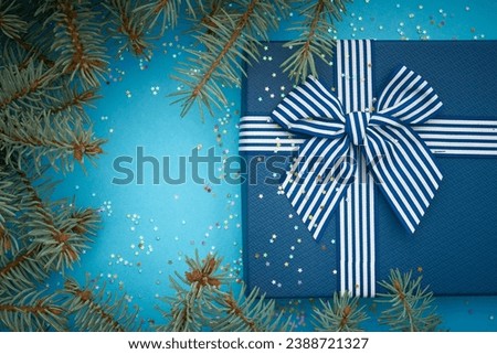 Blue christmas background with blue gift and bow. Textured cover of gift with striped ribbon and bow. Blue paper textured background has a lot of little stars. Empty place for your text with frame 