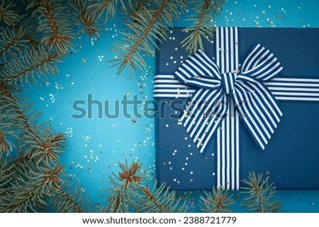 Blue christmas background with blue gift and bow. Textured cover of gift with striped ribbon and bow. Blue paper textured background has a lot of little stars. Empty place for your text with frame