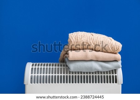 Warm clothes on electric convector heater near blue wall at home. Heating saving concept