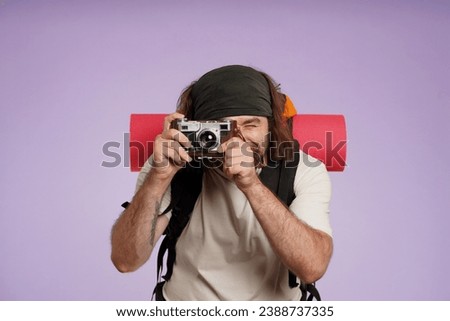 Man tourist in casual clothing with backpack taking photo on old film camera. Isolated on purple background. Portrait of male traveler.