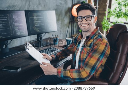 Photo of cheerful successful web designer sitting chair hands hold clipboard paperwork pc screen desktop office indoors