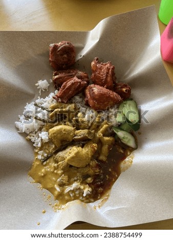 Nasi Kak Wok served on paper. White rice with chicken curry gravy, fried chicken, cucumber and sambal. Famous Malaysia local food. Kelantan Kak Wook Rice. Royalty-Free Stock Photo #2388754499