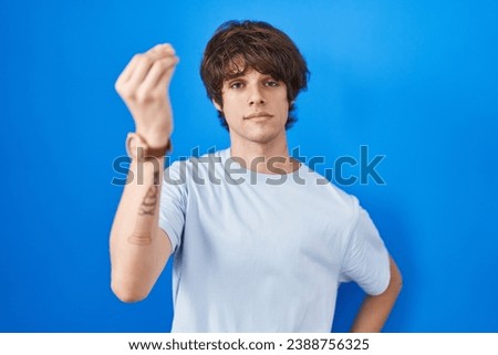 Hispanic young man standing over blue background doing italian gesture with hand and fingers confident expression 