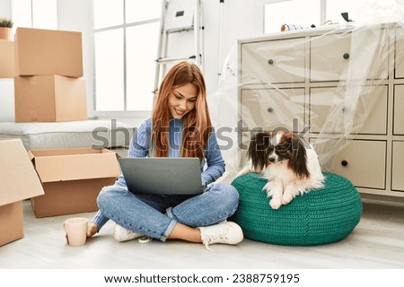 Young caucasian woman using laptop sitting on floor with dog at new home