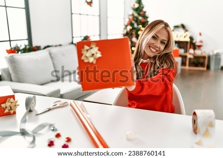 Young caucasian woman holding gift sitting by christmas tree at home Royalty-Free Stock Photo #2388760141