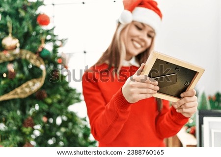Young caucasian woman looking photo standing by christmas tree at home