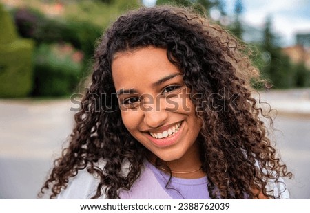 Young hispanic girl smiling at camera outside - Happy female teenager standing in front of school - Portrait of beautiful woman looking at camera outdoors