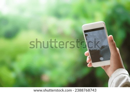 Man hand holding white smartphone phone taking pictures of nature and sky on forest and green plant blurred beautiful background concept of business  and social media.
